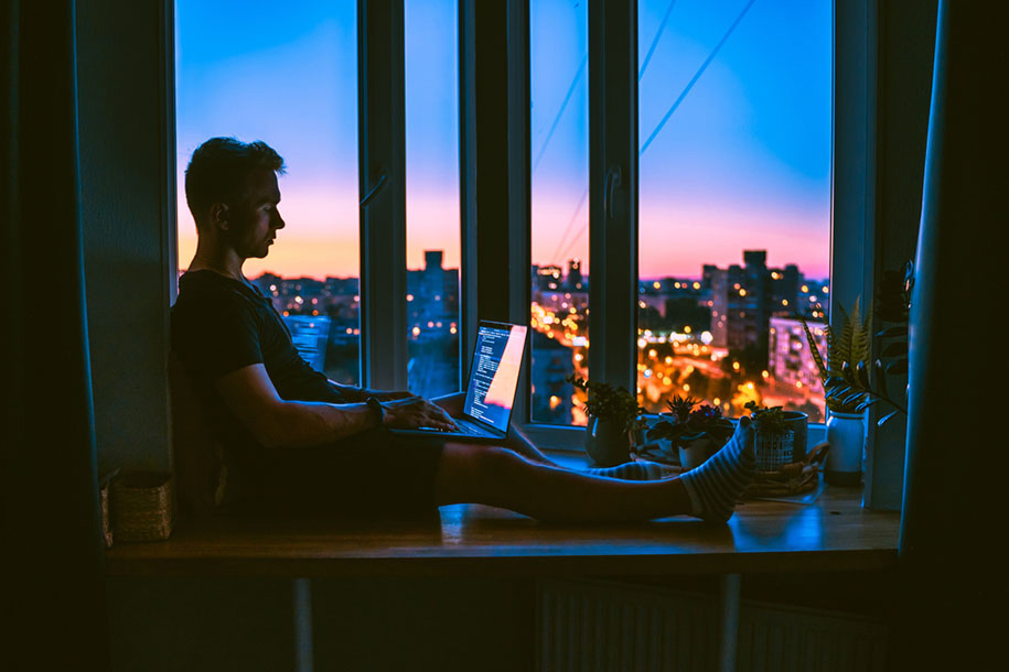 man sitting in a window working on a laptop