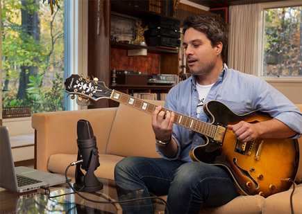 Guy playing guitar into the the Samson Technologies G-Track Pro Professional Streaming USB Microphone