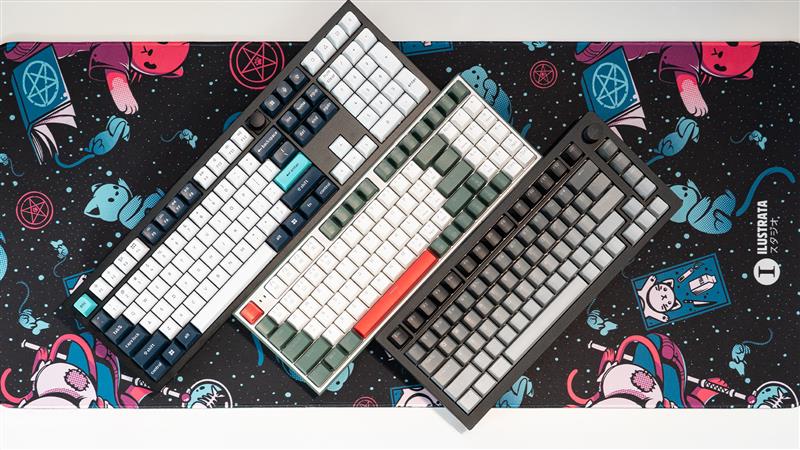 three keyboards of different sizes laid out on top of a cat themed desk mat