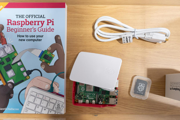 Picture of a Raspberry Pi computer next to a Raspberry Pi beginners guide, cables, and a Pi SD card